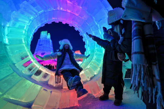 중국 헤이룽장성 하얼빈에서 개막한 '제41회 하얼빈 국제 빙설제'에서 한 방문객이 아름다운 조명으로 빛나는 얼음 조형물 안에서 사진을 찍고 있습니다. AP 연합뉴스